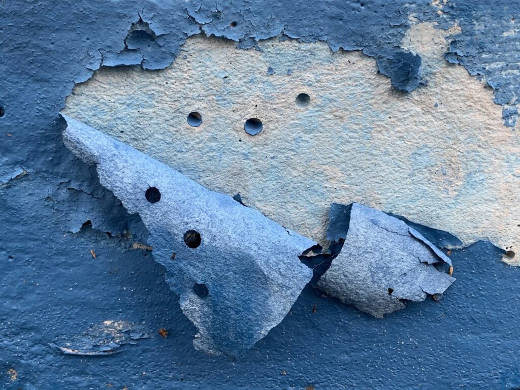 Thick blue paint film peeling and curling off a masonry surface