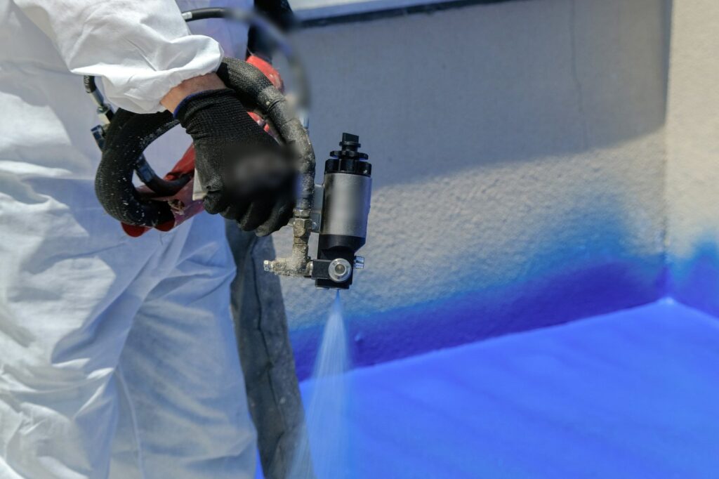 Worker in a protective coverall spraying a blue coating with a plural-component spray gun